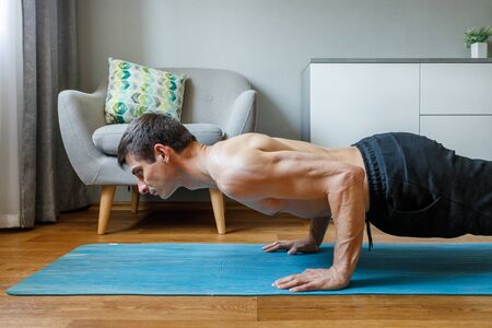 Man in chaturanga pose doing vinyasa flow at home. Practising pilates and yoga at homeの写真素材