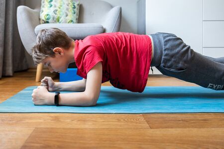 Boy holding forearm plank pose doing yoga at home on quarantineの写真素材