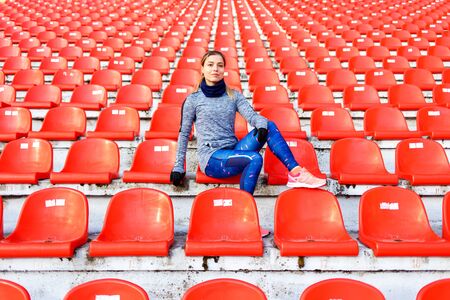 Young sporty runner fitness woman sitting on seats at the stadium