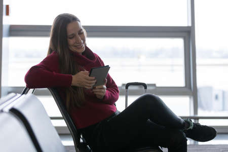 Young woman reading book waiting for the flight at the airport