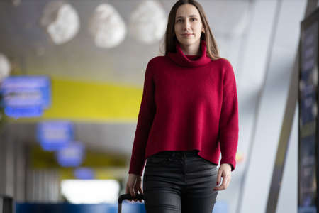 Young traveller woman with her carry-on baggage walking at the airportの写真素材