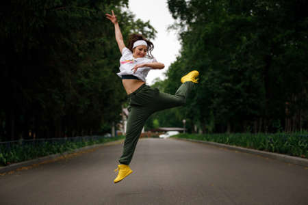 Young fitness girl jumping in dance on the road in the eveningの写真素材