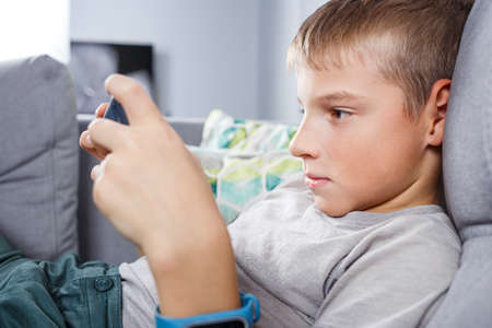 Boy playing games on smartphone sitting at home during quarantineの写真素材