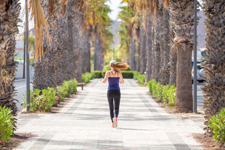 Back view of jogging woman on the street of tropical town. Running girl on summer day