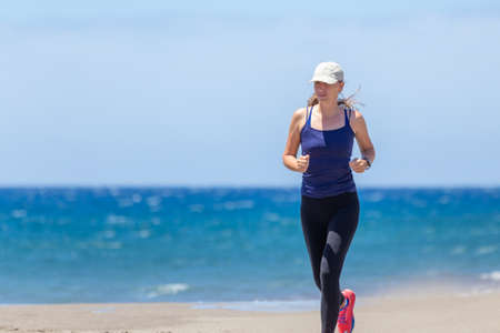 Young slim woman jogging at the ocean beach on sunny day. Fitness girl training running near the seaの写真素材
