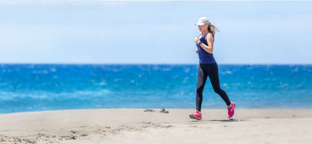 Young slim woman jogging at the ocean beach on sunny day. Fitness girl training running near the seaの写真素材