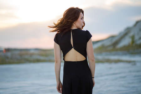 Portrait of young beautiful woman in black dress. Back view