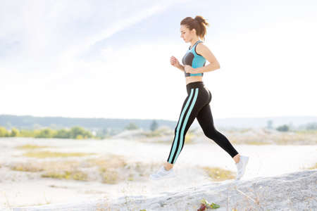Young fitness runner woman jumping on trail path. Slim girl jogging outdoors. Image with copyspace
