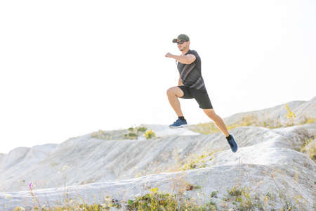 Young sporty runner man jumping from the hill on trail running cross