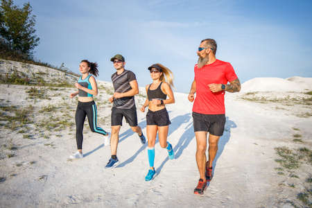 Group of runners jogging outdoors on white terrain. Low wide angle view with long shadows