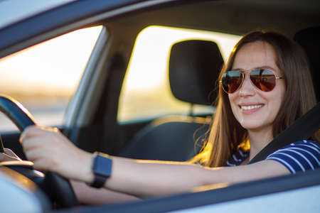 Young woman in sunglasses steering the car at sunset tripの写真素材
