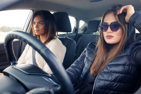 Two young beautiful women travelling in the car. Young female driver with her friend sitting inside a carの写真素材