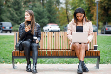 Two different busy women sitting on the bench in the parkの写真素材