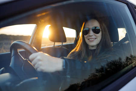 Young woman driving rented or new car in the evening. Automobile rent image backgroundの写真素材