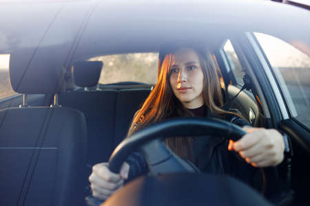 Young woman driving rented or new car in the evening. Automobile rent image backgroundの写真素材