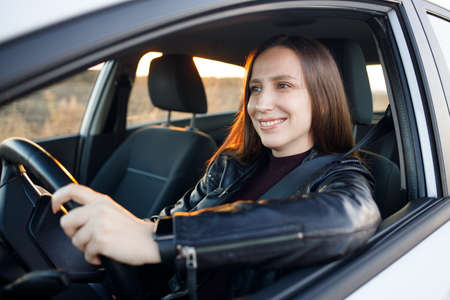 Young woman driving rented or new car in the evening. Automobile rent image backgroundの写真素材