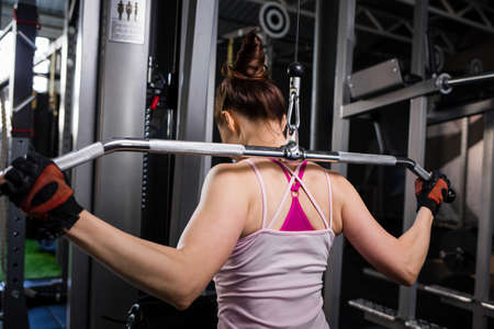 Young fitness woman pulls down weights on cable machine in gym. Wide grip lats pulldown exerciseの写真素材