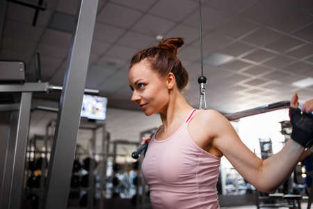 Young fitness woman pulls down weights on cable machine in gym. Wide grip lats pulldown exerciseの写真素材