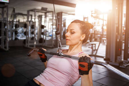 Young sporty woman training her lats and biceps on cable machine in gymの写真素材