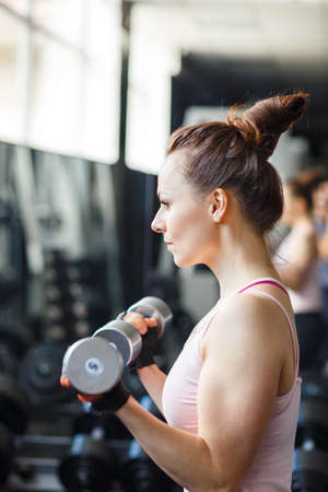 Fitness girl doing exercices with dumbbells for biceps in gymの写真素材