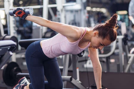 Young sporty woman training her triceps with dumbbells in gymの写真素材