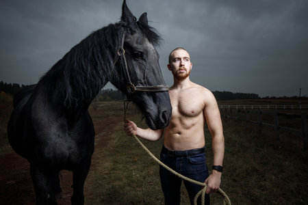 Young strong man with naked torso standing with horse at the countrysideの写真素材