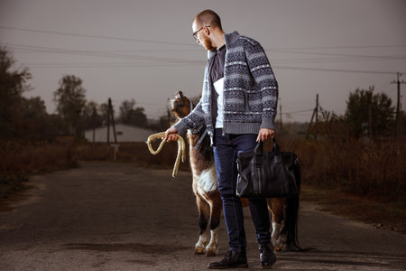 Young student man on his vacation in countryside standing on the road with ponyの写真素材