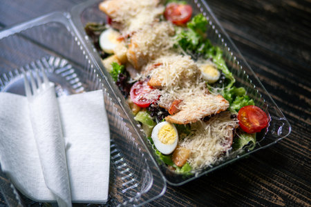 Caesar salad in plastic container for food delivery. Takeaway meal for office workerの写真素材