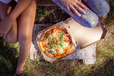Two teenage girls sitting outdoor with pizza. Delivery pizza concept imageの写真素材