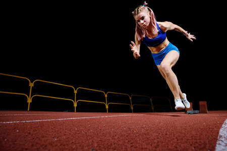 Female track runner bursting off starting block against black backgroundの写真素材