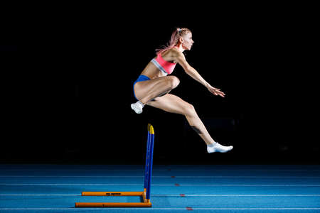 Young sportwoman jumps over the hurdle on sprint runの写真素材