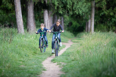 Girl and her younger brother ride bicycles in parkの写真素材