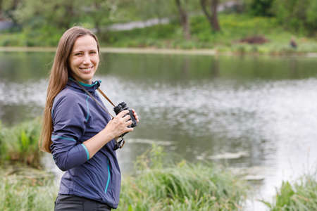 Young woman standing with binoculars near the pondの写真素材