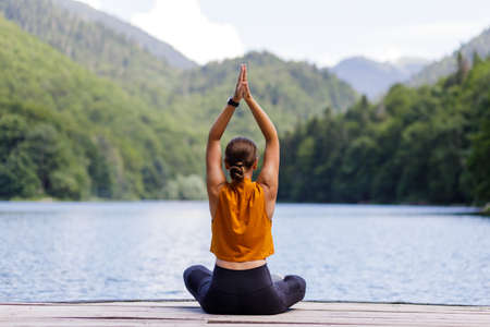 Young woman meditating or practicing yoga at the lake in the mountains.の写真素材