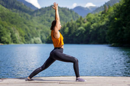 Young woman doing warrior yoga pose near the lake.の写真素材