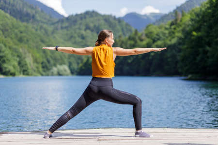 Young woman doing warrior yoga pose near the lake.の写真素材