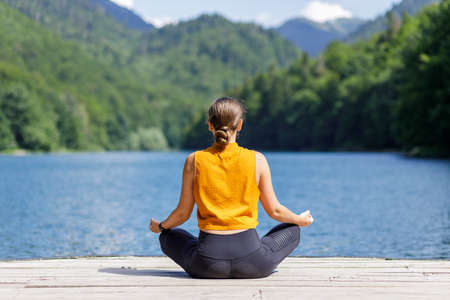 Young woman meditating or practicing yoga at the lake in the mountains.の写真素材
