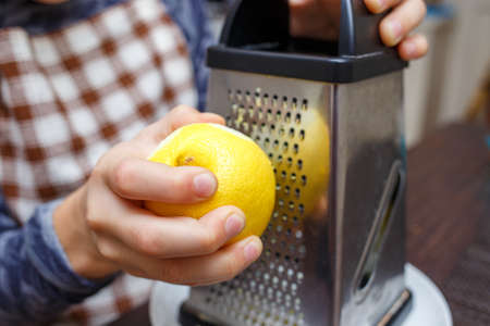 Young boy zesting lemon with grater at home kitchen. Home cooking learning kidの写真素材