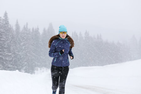 Young slim woman running on the road in the winter snowy morning. Close up portrait of jogging fitness woman with copy space.の写真素材
