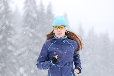 Young slim woman running on the road in the winter snowy morning. Close up portrait of jogging fitness woman.の写真素材