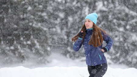 Young pretty woman jogging in winter park. Outdoors cold weather running lifestyle background with copy space.の写真素材
