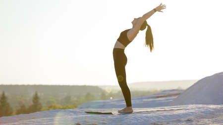 Young fitness woman doing yoga outdoors at sunset. backbend stretching trainingの写真素材