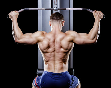 Back view of young topless bodybuilder works out pulling down on cable machine in gymの写真素材