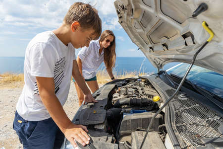 Teenage boy with his mother trying to fix broken rent car during summer vacation. Rent car insurance concept imageの写真素材