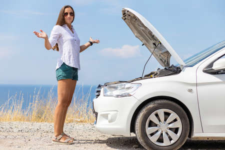 Young slim woman standing embarrassed near her car during summer vacationの写真素材