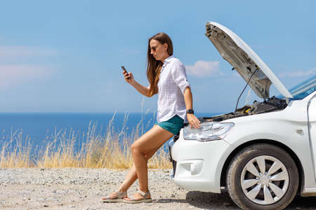 Young woman standing near broken car and calling car servise or insurance companyの写真素材