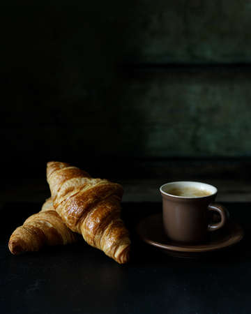 Cup of hot coffee with two fresh croissants against dark background.の写真素材