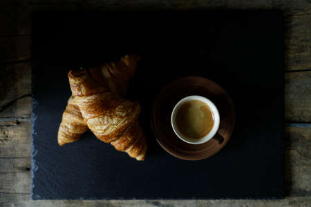 Cup of hot coffee with two fresh croissants against dark background.の写真素材
