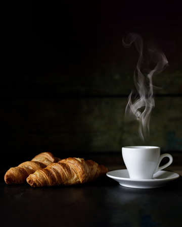 Cup of espresso with two fresh croissants against dark background.の写真素材