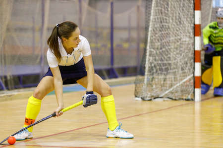 Young female player performing penalty shot in indoor hockey game